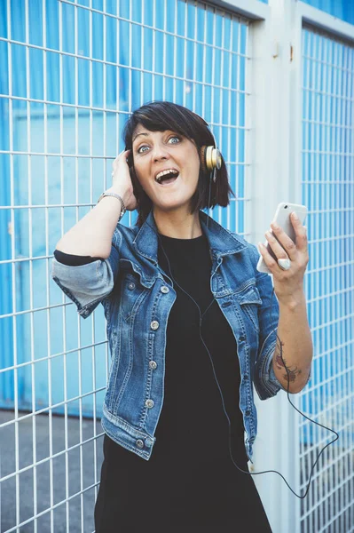 Brunett tjej med hörlurar och smartphone på gatan — Stockfoto