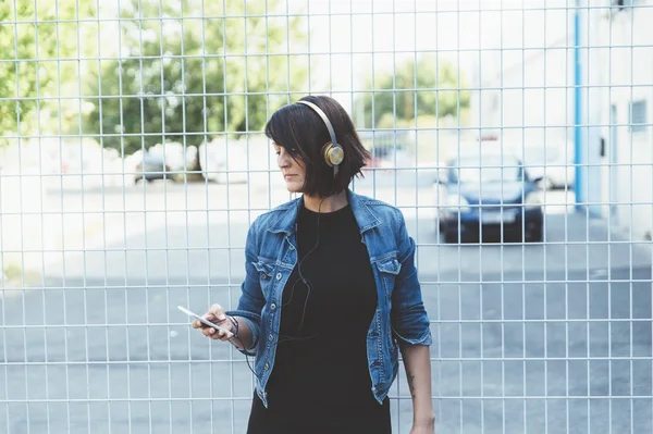 Brünettes Mädchen mit Kopfhörer und Smartphone auf der Straße — Stockfoto