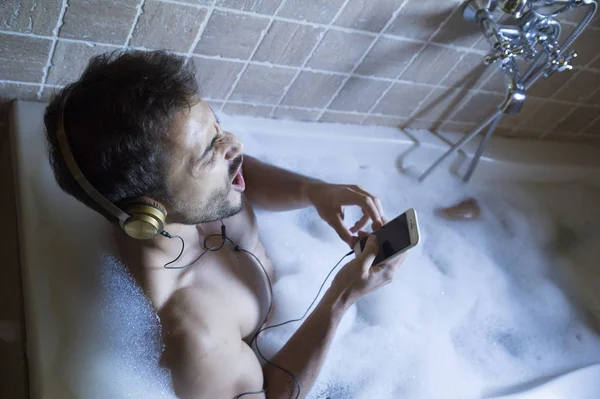 Nøgen fyr i badeværelse med smartphone og hovedtelefoner - Stock-foto