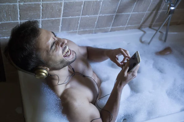 Голий хлопець у ванній кімнаті з смартфоном та навушниками — стокове фото