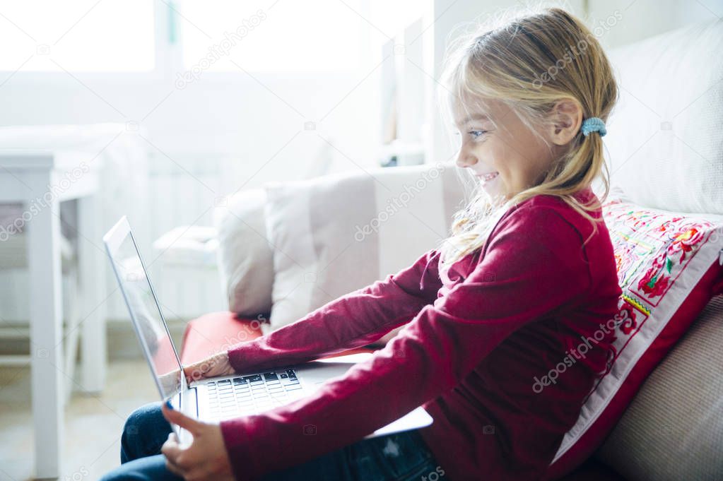 Happy  little girl lying on the sofa with laptop in the living r