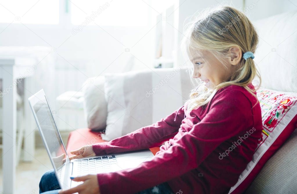 Happy  little girl lying on the sofa with laptop in the living r