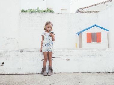 Küçük güzel kız telefonu sahiptir. O kulaklıklar. 