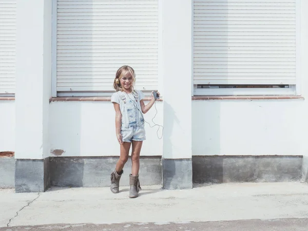 Pequena menina bonita gosta do telefone. Ela fones de ouvido . — Fotografia de Stock