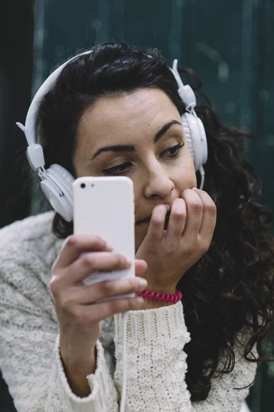 Muchacha atractiva escuchando música con smartphone y oído blanco —  Fotos de Stock