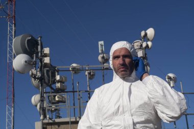 Beyaz bir giysi ve mavi eldiven, anten telefonla konuşan adam