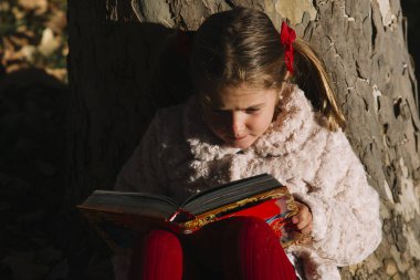 Güzel küçük bir kız parkta bir kitap okuma