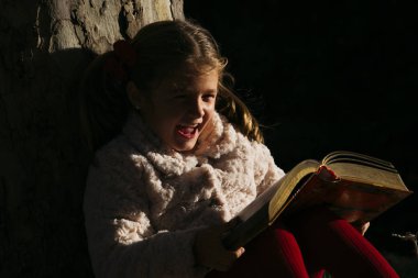 Güzel küçük bir kız parkta bir kitap okuma