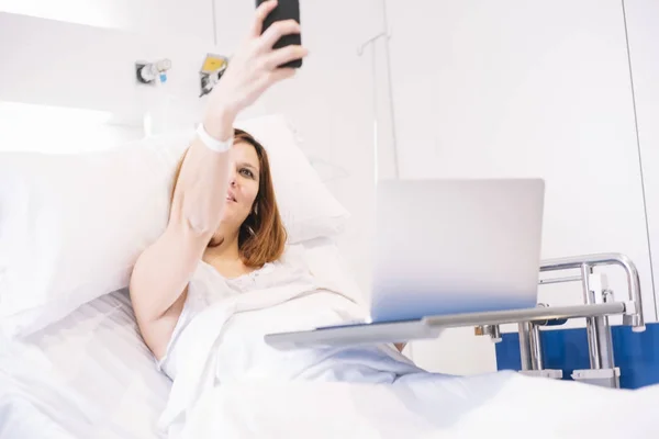 Donna malata con smartphone e laptop in ospedale — Foto Stock