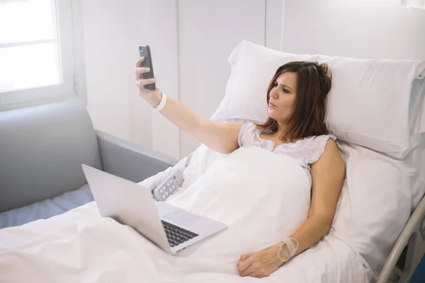 Donna malata con smartphone e laptop in ospedale — Foto Stock