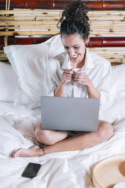 Όμορφη γυναίκα με τηλέφωνο και φορητό υπολογιστή στο κρεβάτι — Φωτογραφία Αρχείου