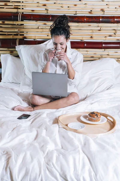 Flot kvinde med telefon og laptop i sengen - Stock-foto