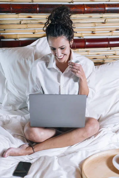 Flot kvinde med telefon og laptop i sengen - Stock-foto