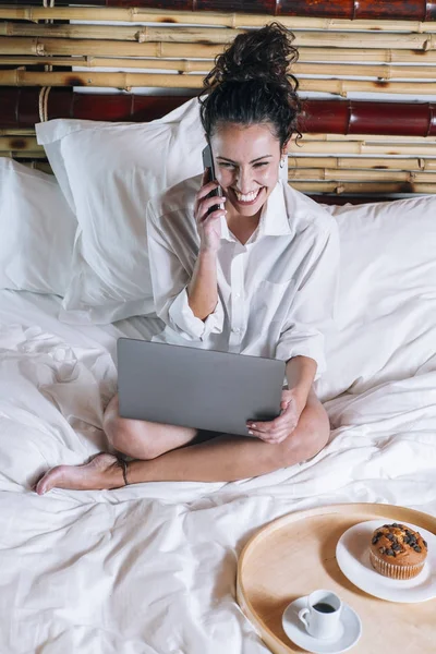 Bella donna con telefono e laptop a letto — Foto Stock