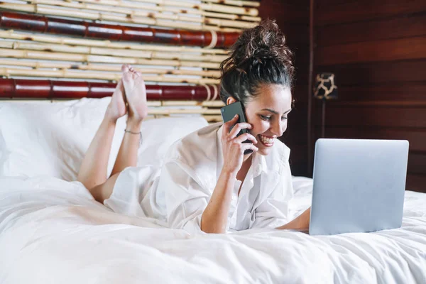 Bella donna con telefono e laptop a letto — Foto Stock