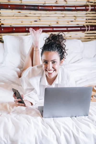 Bella donna con telefono e laptop a letto — Foto Stock