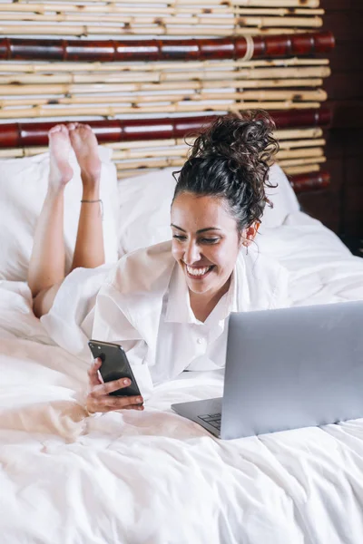Красивая женщина с телефоном и ноутбуком в постели — стоковое фото