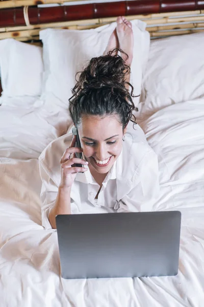 Bella donna con telefono e laptop a letto — Foto Stock