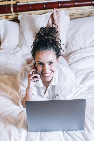 Bella donna con telefono e laptop a letto — Foto Stock