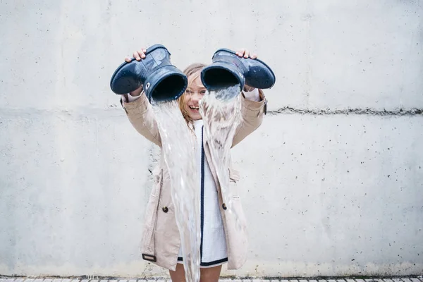 Menina derramando água de sua bota e jogando na chuva . — Fotografia de Stock