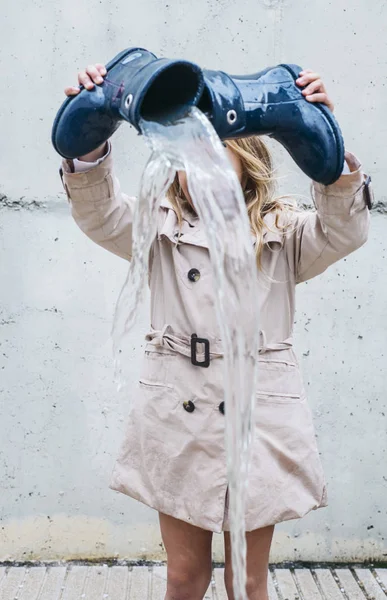 Menina derramando água de sua bota e jogando na chuva . — Fotografia de Stock