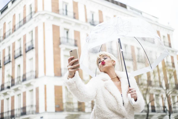 Blonde woman with umbrella texting on smartphone — Stock Photo, Image