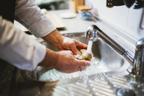 Hombre de 59 años lava el tomate en la cocina de su casa . — Foto de Stock