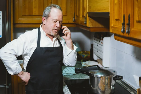 Homme de 59 ans avec smartphone dans la cuisine de sa maison . — Photo