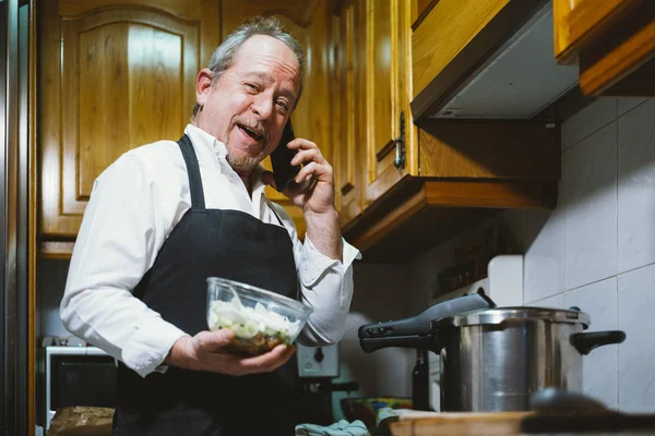 Homme de 59 ans avec smartphone dans la cuisine de sa maison . — Photo
