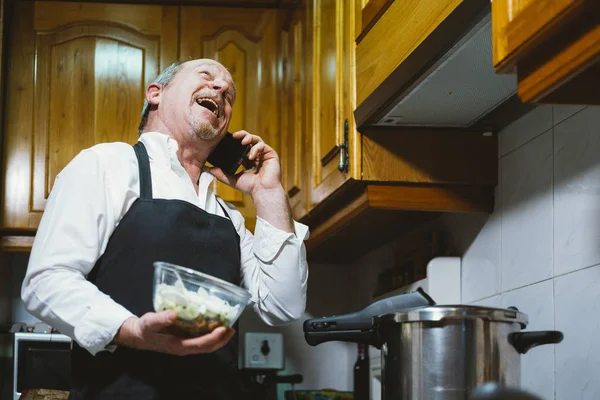 Homme de 59 ans avec smartphone dans la cuisine de sa maison . — Photo