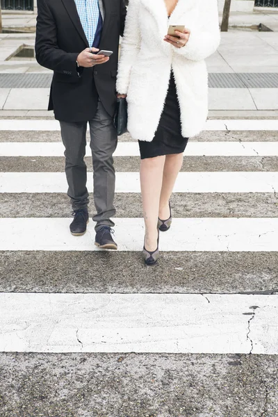 Homem e mulher caminhando no cruzamento zebra com smartphone — Fotografia de Stock