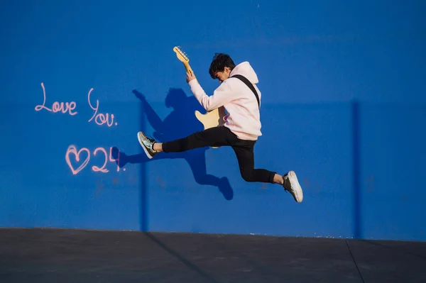 Молодий чоловік стрибає з електричною гітарою на синьому фоні — стокове фото