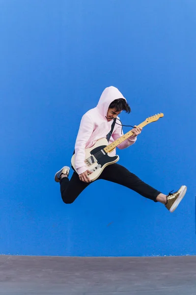 Jovem saltando com guitarra elétrica no fundo azul — Fotografia de Stock