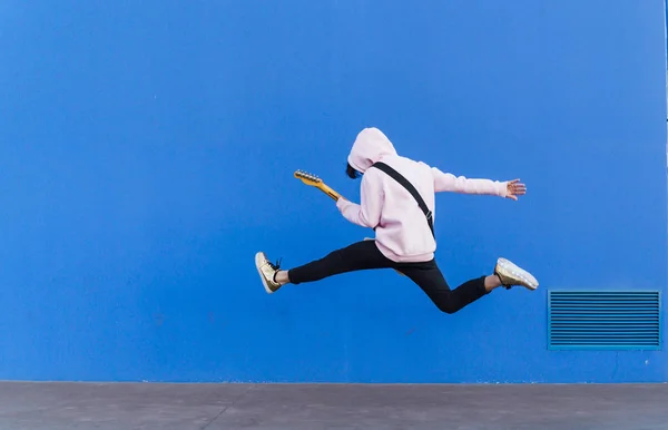 青い背景にエレキギターで飛び跳ねる青年 — ストック写真