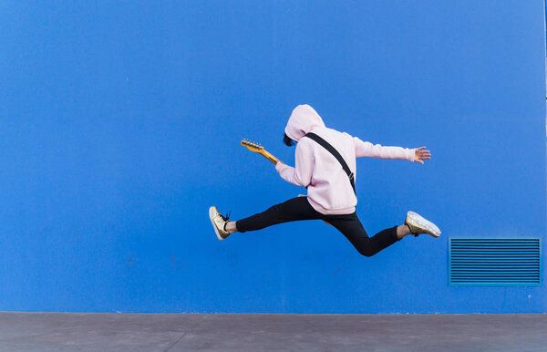 young man jumping with electric guitar on blue background