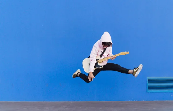 Young man jumping with electric guitar on blue background — Stock Photo, Image