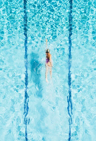 Une femme nage dans une piscine, vue d'en haut. Elle a l'air minuscule dans l'immense piscine . — Photo