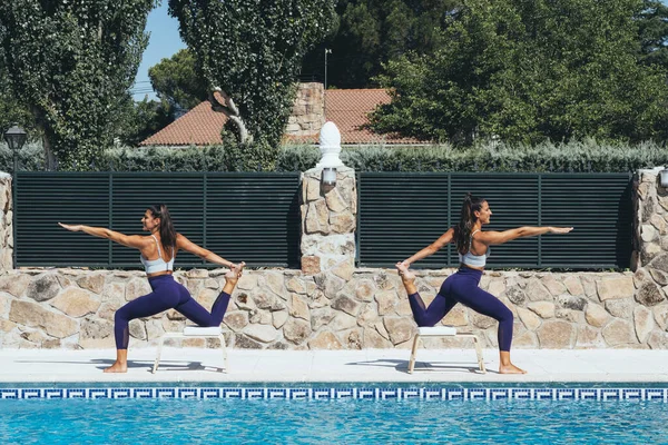 Hermanas gemelas practicando yoga junto a una piscina . — Foto de Stock