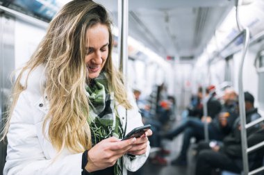 Kadın akıllı telefonuyla metroda seyahat ediyor.