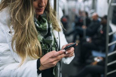 Kadın akıllı telefonuyla metroda seyahat ediyor.