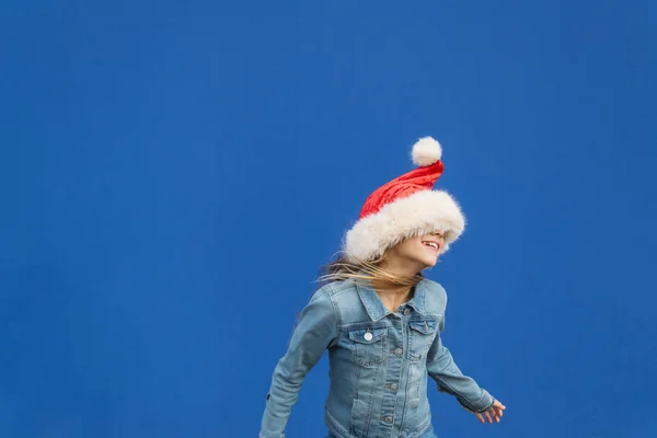 Ένα ξανθό κοριτσάκι που χορεύει με ένα καπέλο Αϊ Βασίλη. Καλά Χριστούγεννα.! — Φωτογραφία Αρχείου