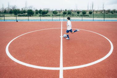 Futbolcu çocuk topa vuruyor.