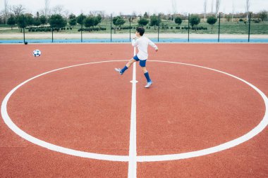 Futbolcu çocuk topa vuruyor.
