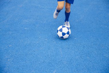 Mavi arka planda futbol oynayan tanınmayan küçük çocuk.