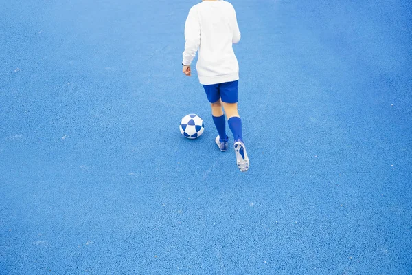 Маленький невпізнаваний хлопчик грає у футбол синього фону — стокове фото