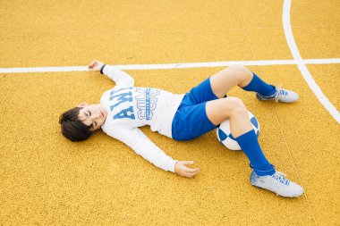 Futbolcu çocuk sahada yatıyor.