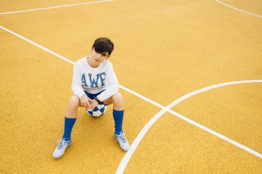 Topun üzerinde oturan futbolcu çocuğun portresi.