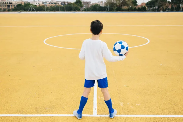 Назад хлопчика-футболіста, який тримає м'яч вручну — стокове фото