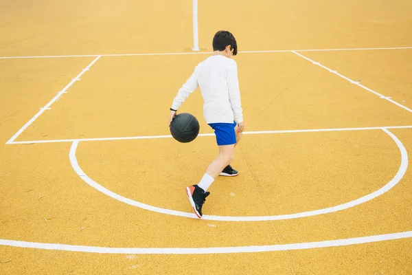 Молодий хлопчик грає на жовтому баскетбольному майданчику на відкритому повітрі . — стокове фото