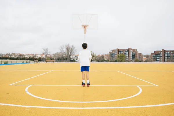 Jonge jongen spelen op gele basketbalveld outdoor. — Stockfoto
